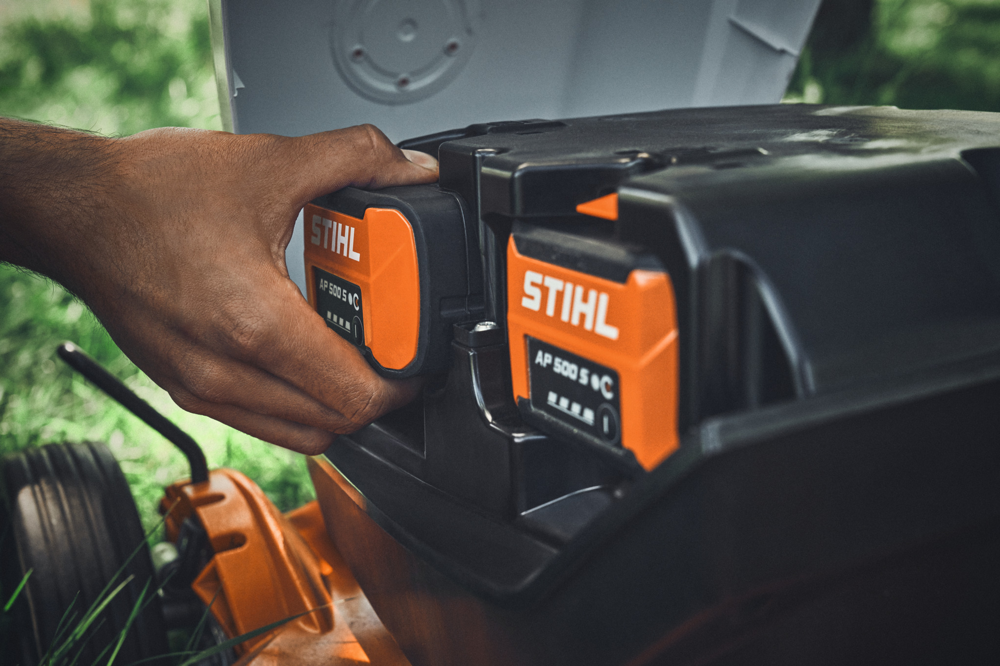 En person sætter et STIHL AP 500 S batteri i en STIHL batteridrevet plæneklipper