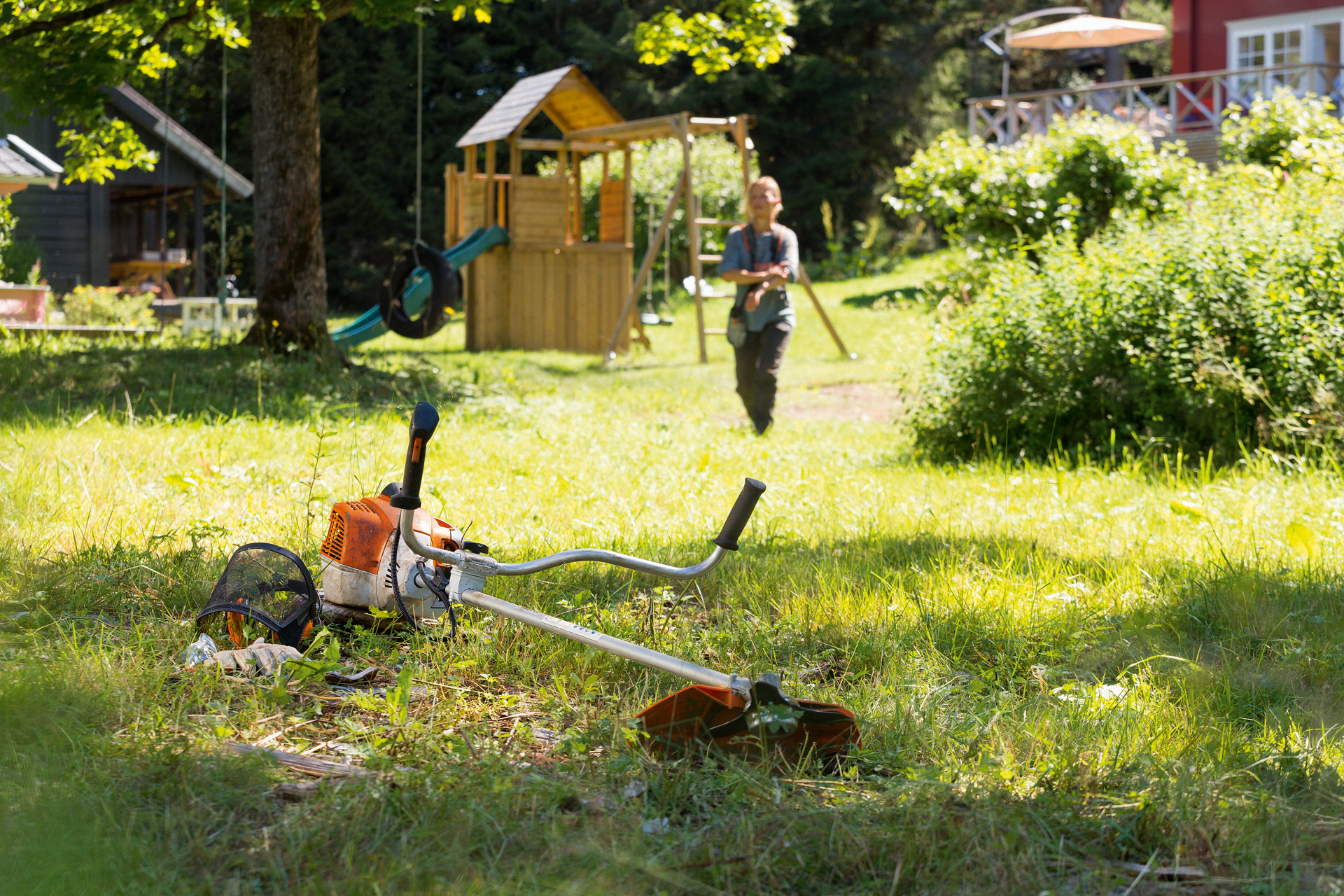 En STIHL FS 240 buskrydder i græs med en mand, der forbereder vedligeholdelse i baggrunden.